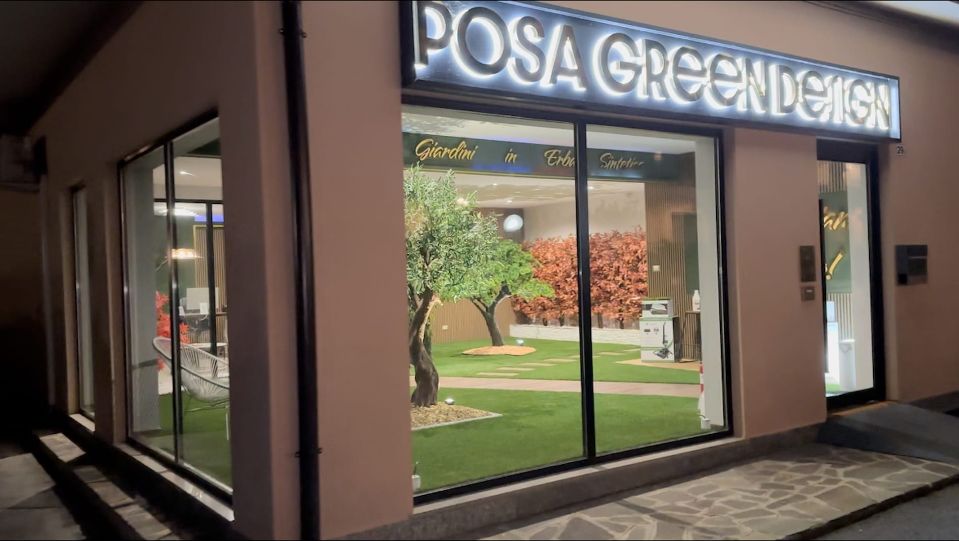 Vista esterna del negozio Posa Green Design. Showroom illuminato dedicato a giardini in erba sintetica con esposizione di prodotti e soluzioni per spazi verdi senza manutenzione.